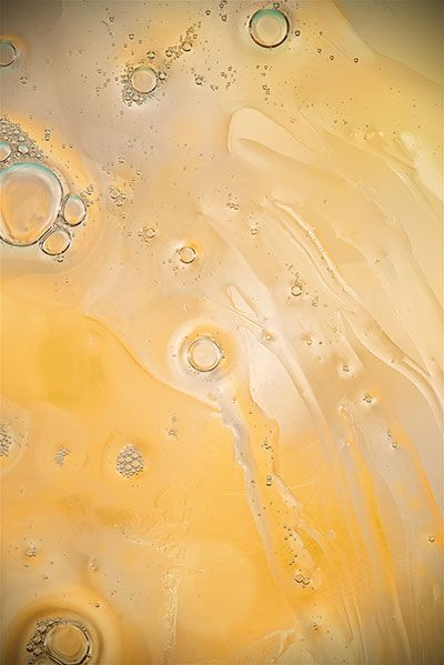 Nahaufnahme von gelb-orangefarbenen Flüssigkeiten mit Blasen und schimmernden Reflexen auf der Oberfläche