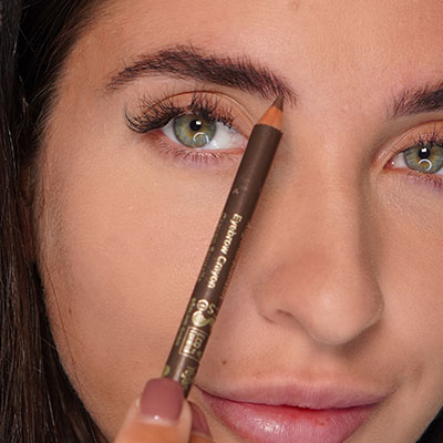 Frau hält braunen Augenbrauenstift nah an ihre Augenbraue, Fokus auf präzises Nachzeichnen der Braue