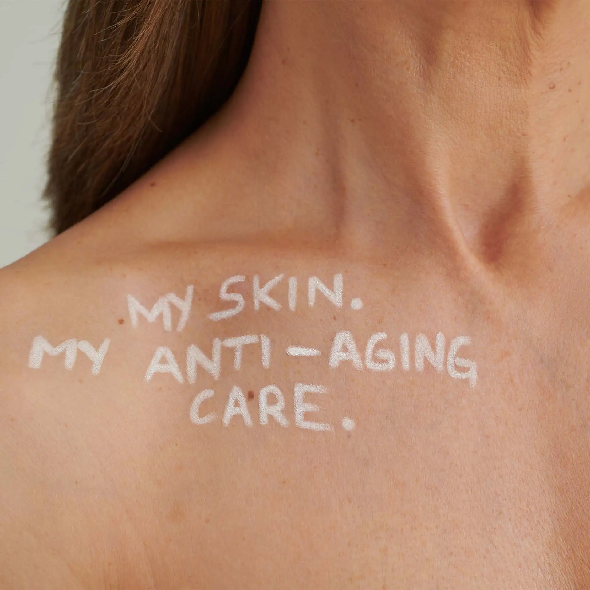 Schulter und Hals einer Person mit weißem Schriftzug „MY SKIN. MY ANTI-AGING CARE.“ auf der Haut