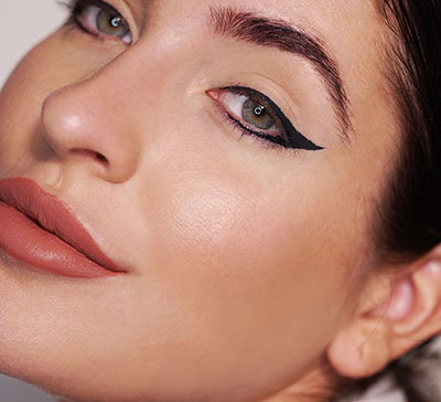 Nahaufnahme eines Gesichts mit rundem Auge und präzisem, schwarzem Lidstrich, natürlicher Lippenfarbe