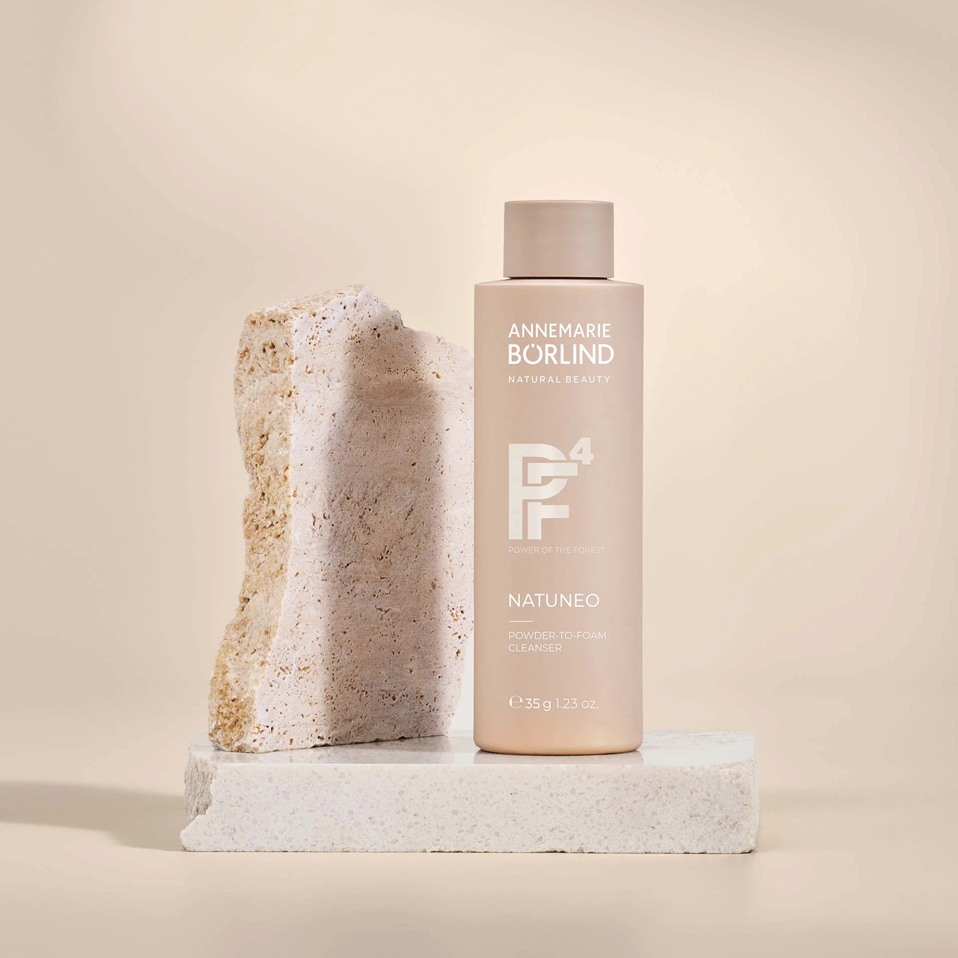ANNEMARIE BÖRLIND NATUNEO Powder-to-Foam Cleanser in beige Flasche neben hellem Naturstein auf Steinplatte