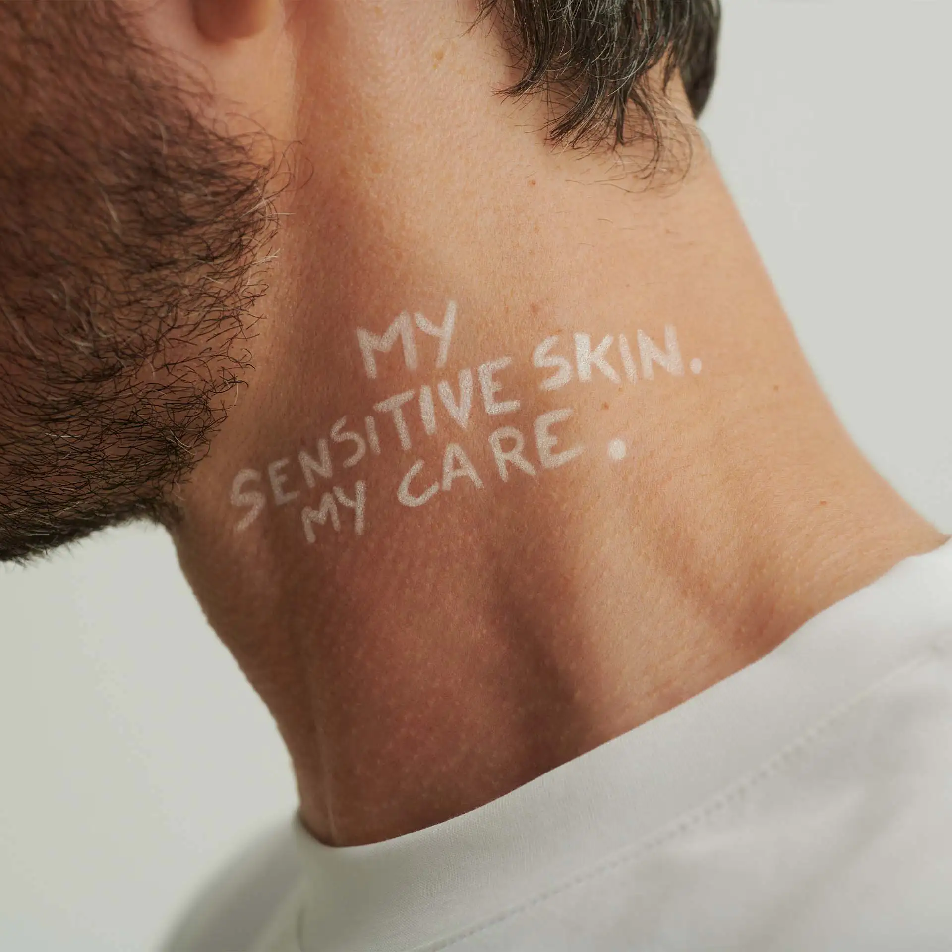 Hals eines Mannes mit Bart, weißer Schriftzug "MY SENSITIVE SKIN. MY CARE." auf der Haut