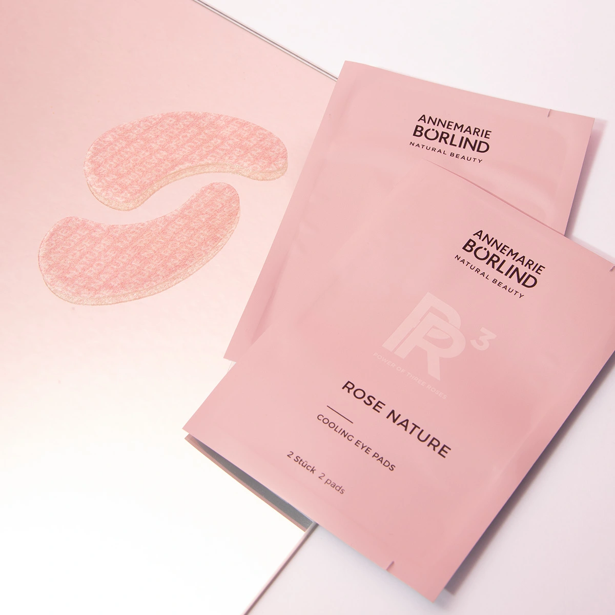ANNEMARIE BÖRLIND ROSE NATURE Cooling Eye Pads in rosa Verpackung mit zwei Pads neben Spiegeloberfläche