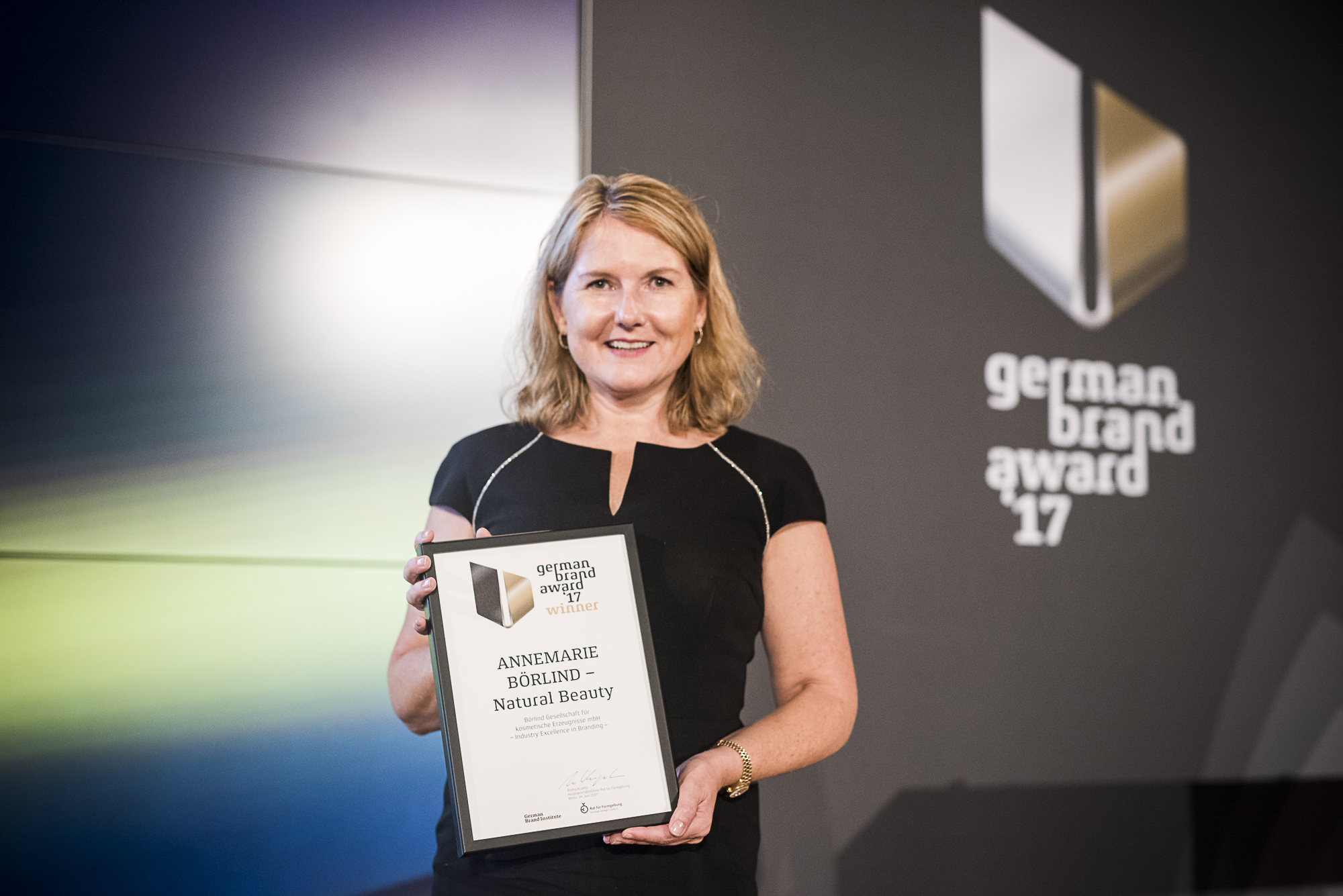Frau hält Urkunde für ANNEMARIE BÖRLIND Natural Beauty beim German Brand Award 2017 vor Logo-Wand