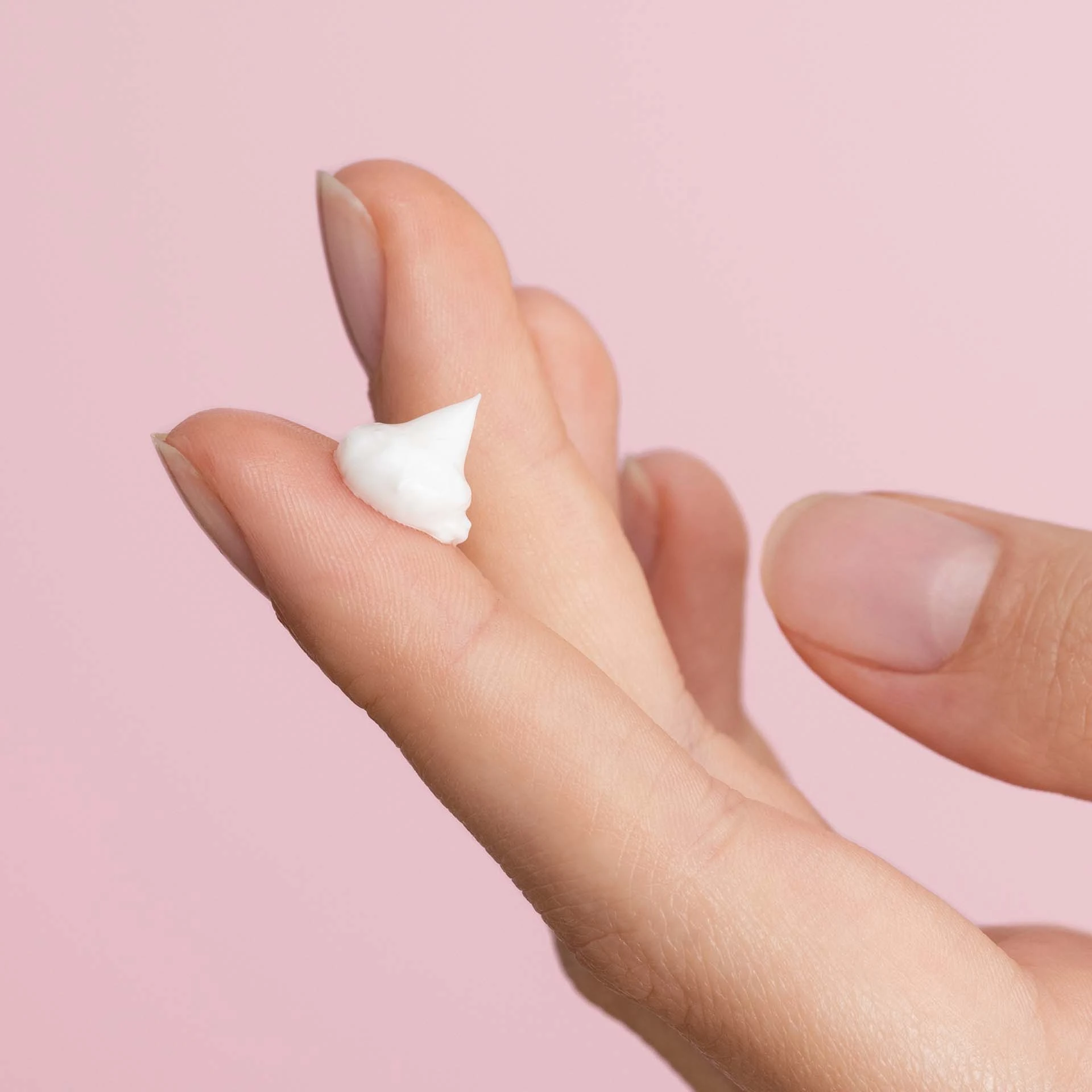 DADO SENS EXTRODERM Augencreme-Textur auf Finger vor rosa Hintergrund, cremig und weiß