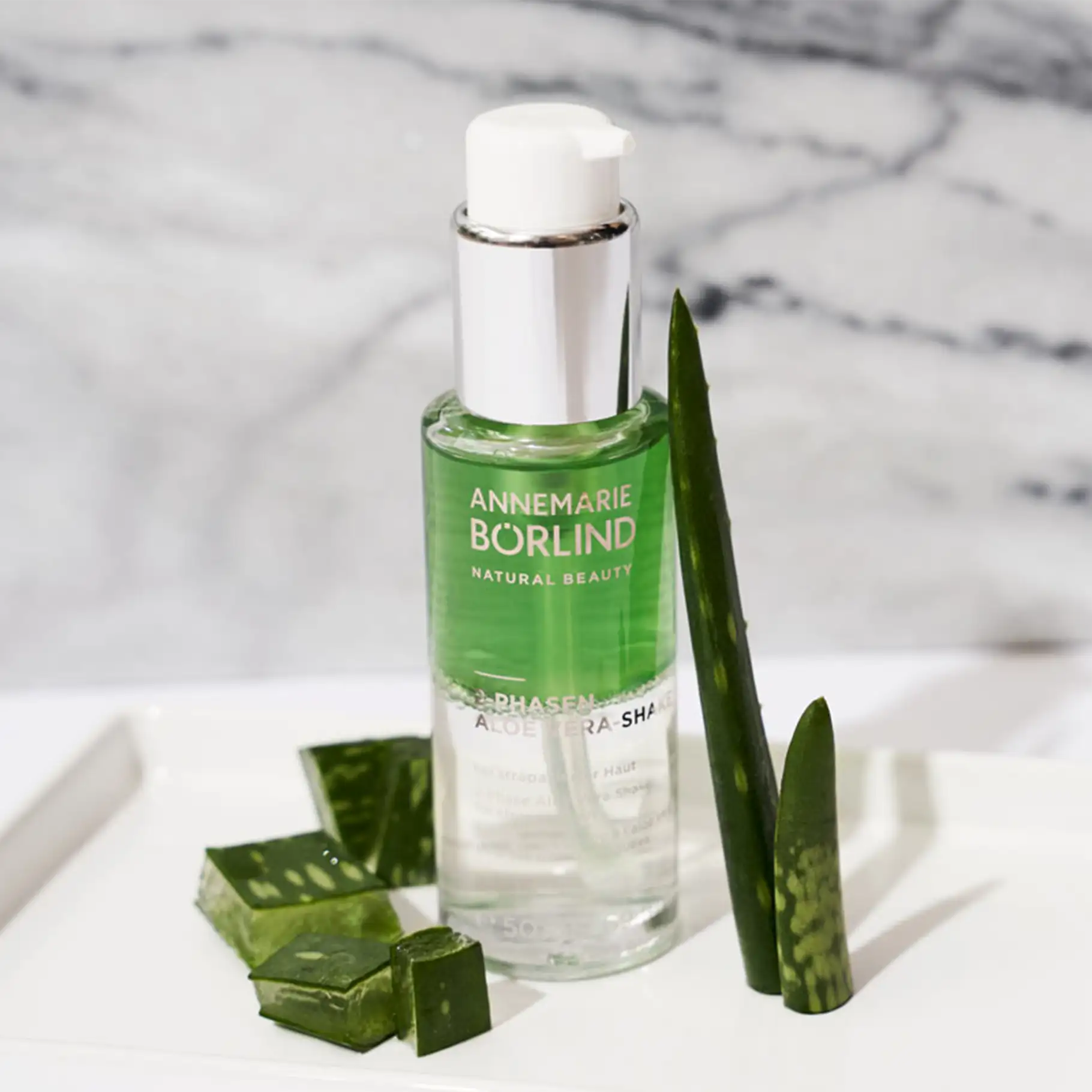 ANNEMARIE BÖRLIND 2-Phasen Aloe Vera Shake mit grünem Gel und Aloe Vera Pflanzenteilen auf weißem Untergrund