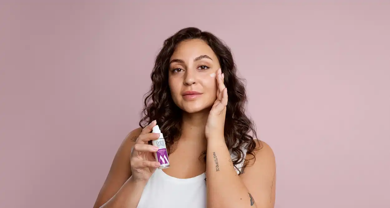 Frau trägt DADO SENS Gesichtscreme auf Wange auf vor rosa Hintergrund