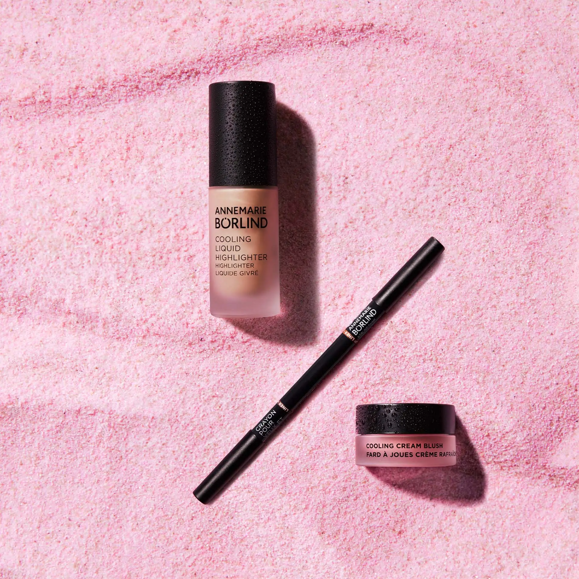 ANNEMARIE BÖRLIND Cooling Liquid Highlighter, Cream Blush und schwarzer Eyeliner auf rosa Puderfläche