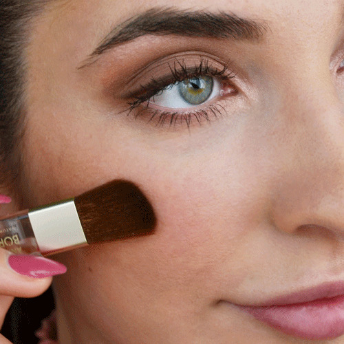 Nahaufnahme einer Frau, die mit einem Pinsel Rouge auf die Wange aufträgt, natürlicher Look