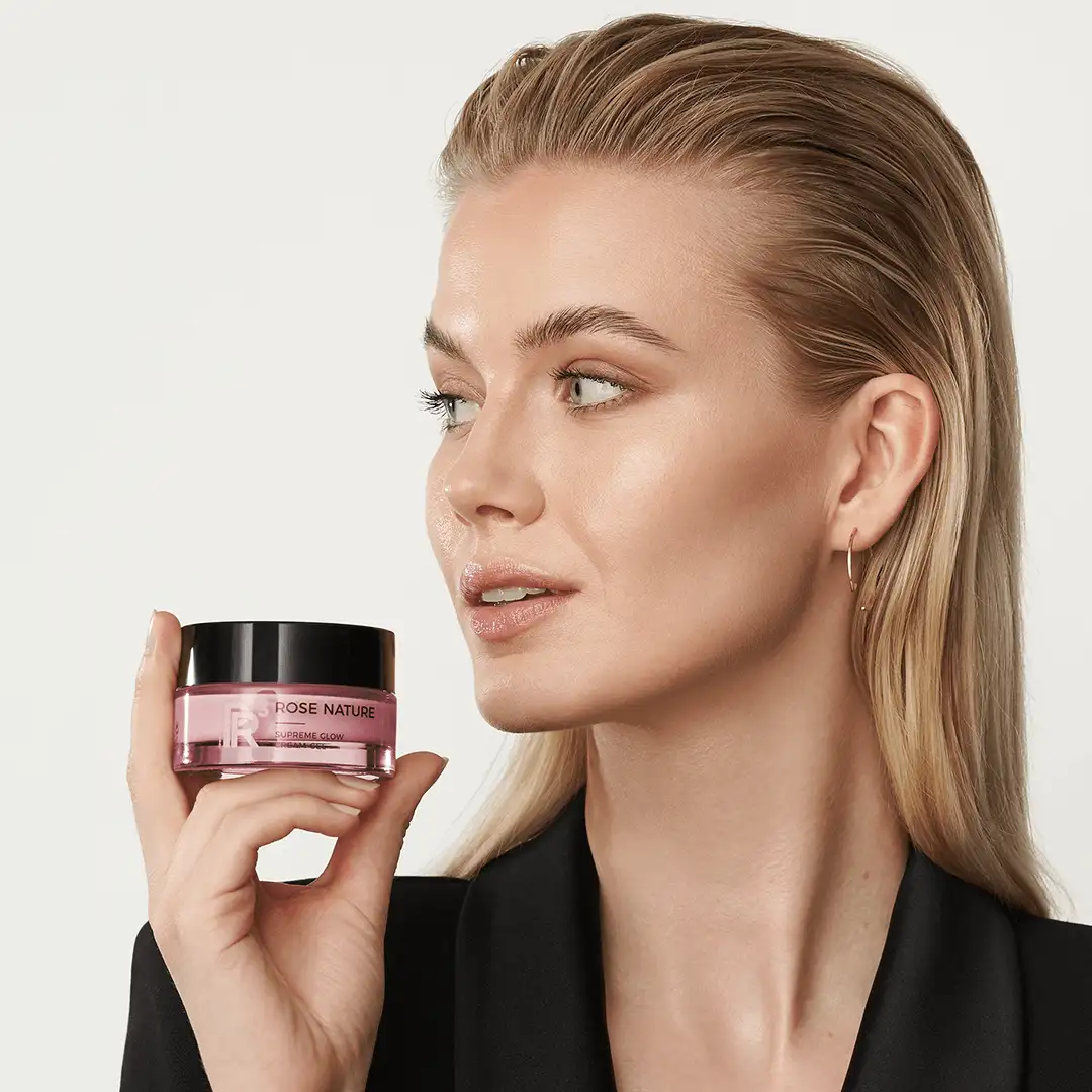 Frau hält ROSE NATURE Supreme Glow Cream-Gel in der Hand, Blick seitlich, glatte Haut, dezentes Make-up