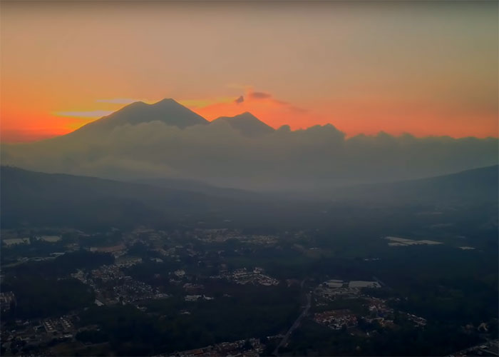 Vulkane bei Sonnenuntergang mit orangefarbenem Himmel und Wolken über einer Stadtlandschaft in Guatemala