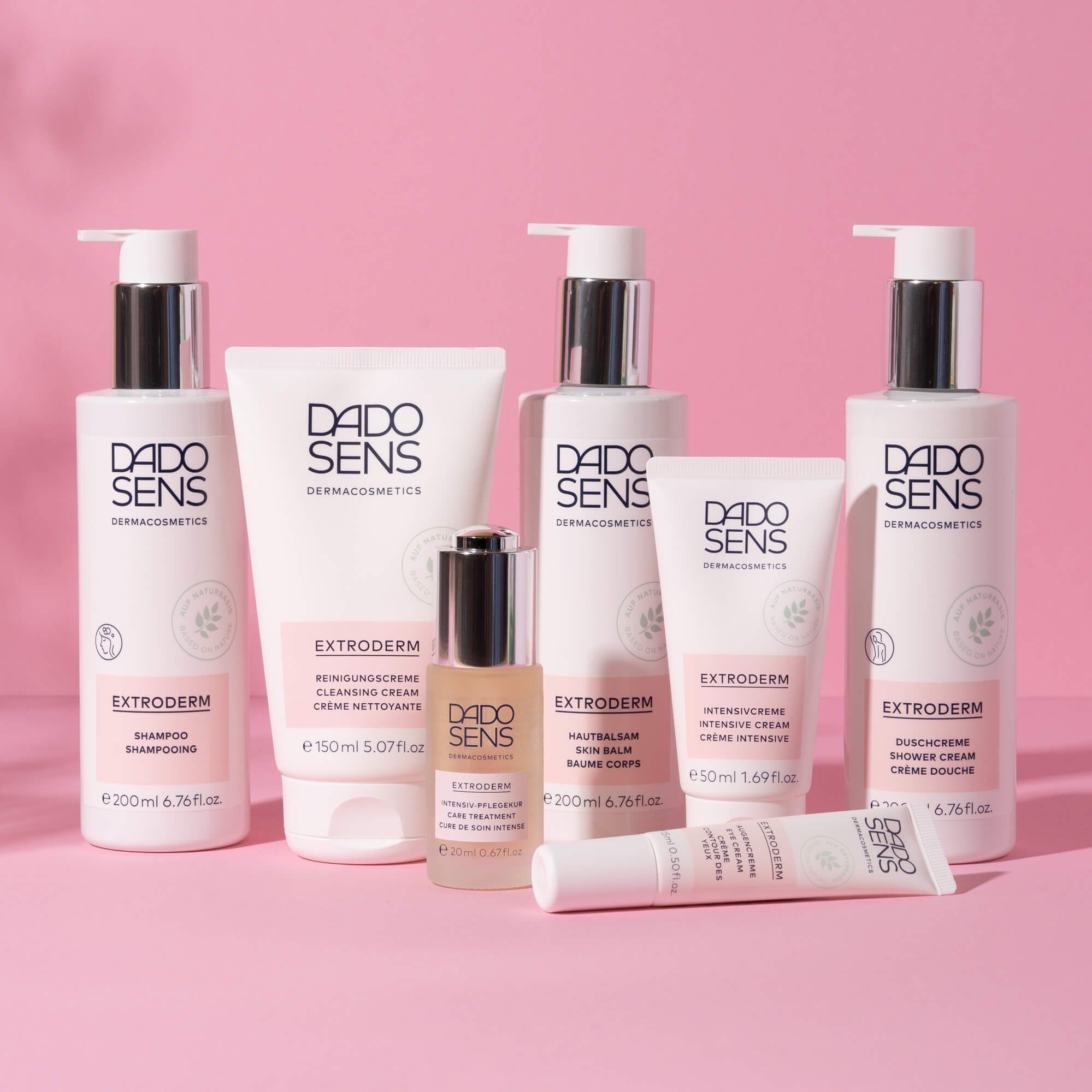 DADO SENS EXTRODERM Pflegeprodukte mit Shampoo, Reinigungscreme, Hautbalsam, Intensivcreme und Duschcreme vor rosa Hinterg...