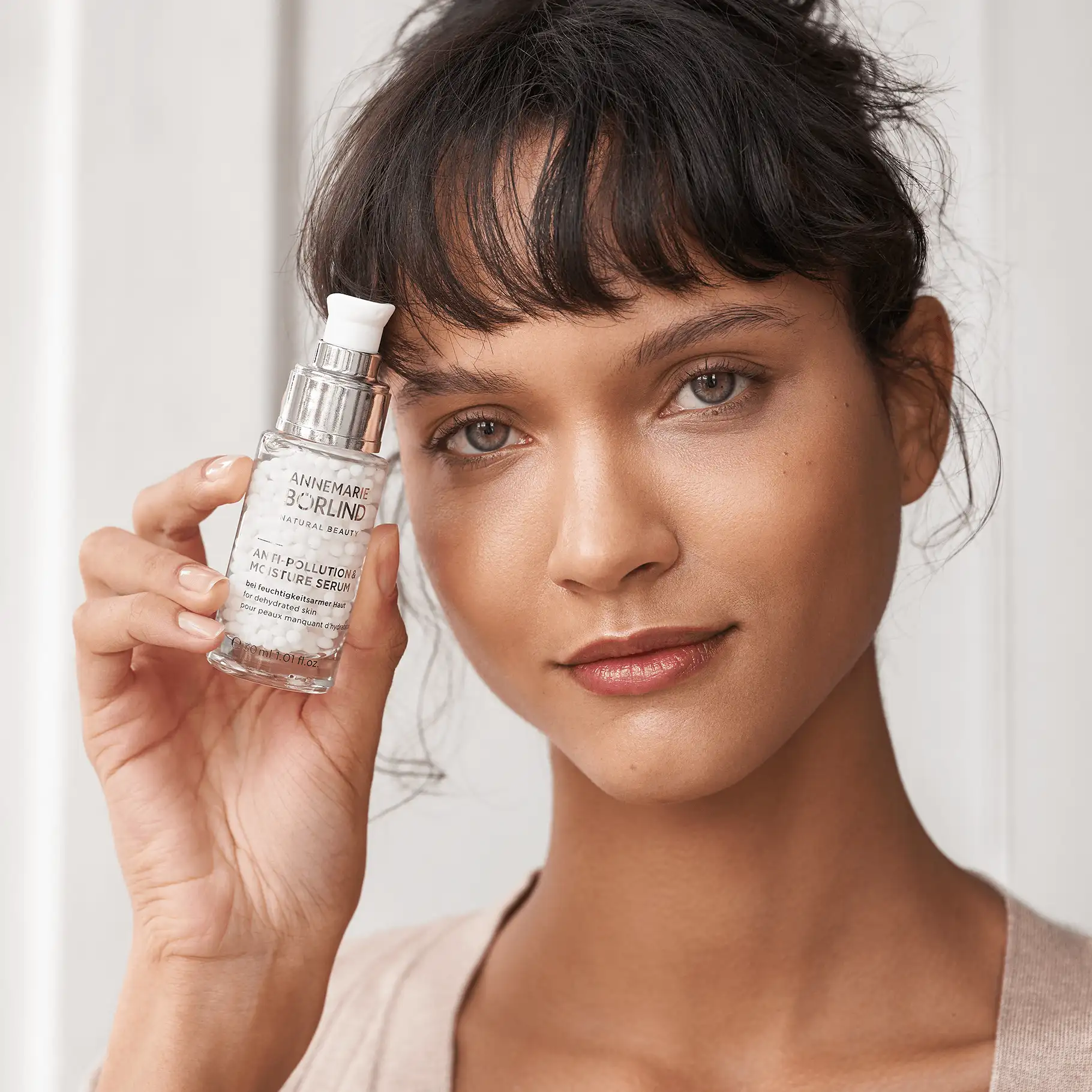 Frau hält ANNEMARIE BÖRLIND Anti-Pollution & Moisture Serum mit weißen Perlen in Glasflasche
