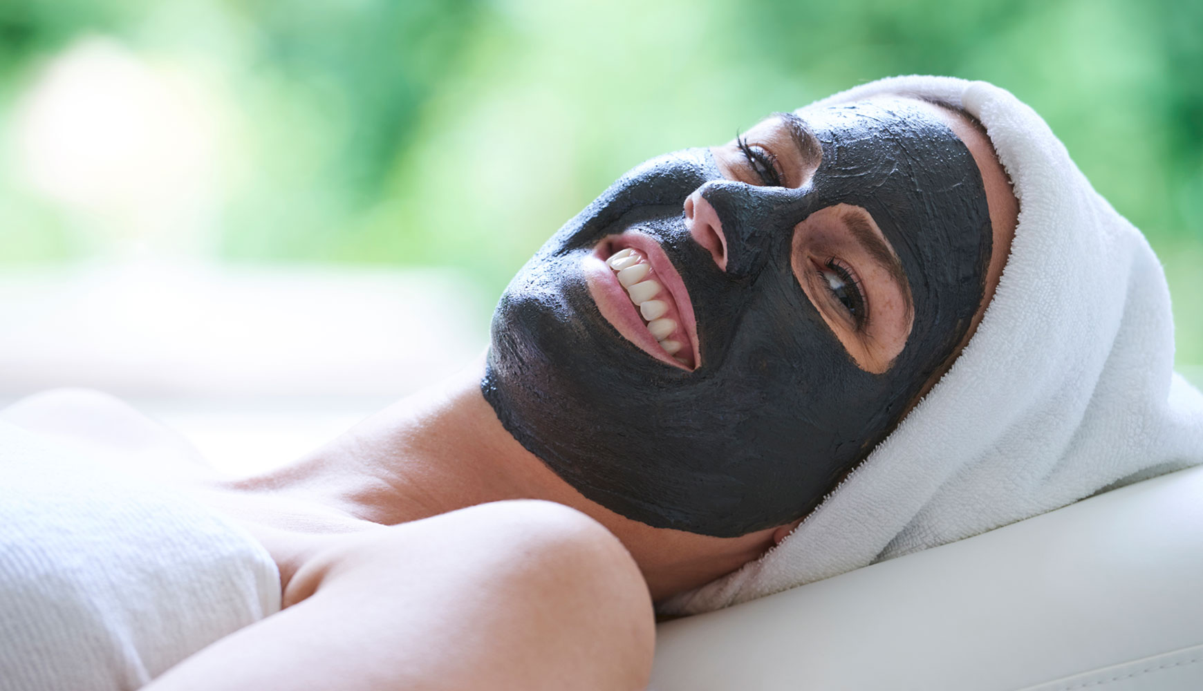 Frau entspannt liegend mit schwarzer Gesichtsmaske und Handtuch um den Kopf in hellem Spa-Ambiente