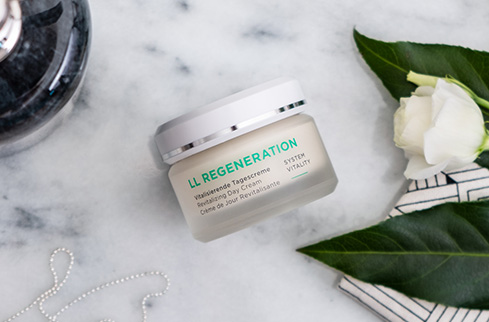 LL REGENERATION vitalisierende Tagescreme im Tiegel auf Marmor mit weißer Blüte und grünem Blatt