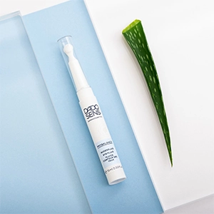 Augencreme für empfindliche Augen: DADO SENS PROBALANCE Augenfluid mit Applikator, inszeniert auf blau-weißem Untergrund neben einem frischen Aloe-vera-Blatt.