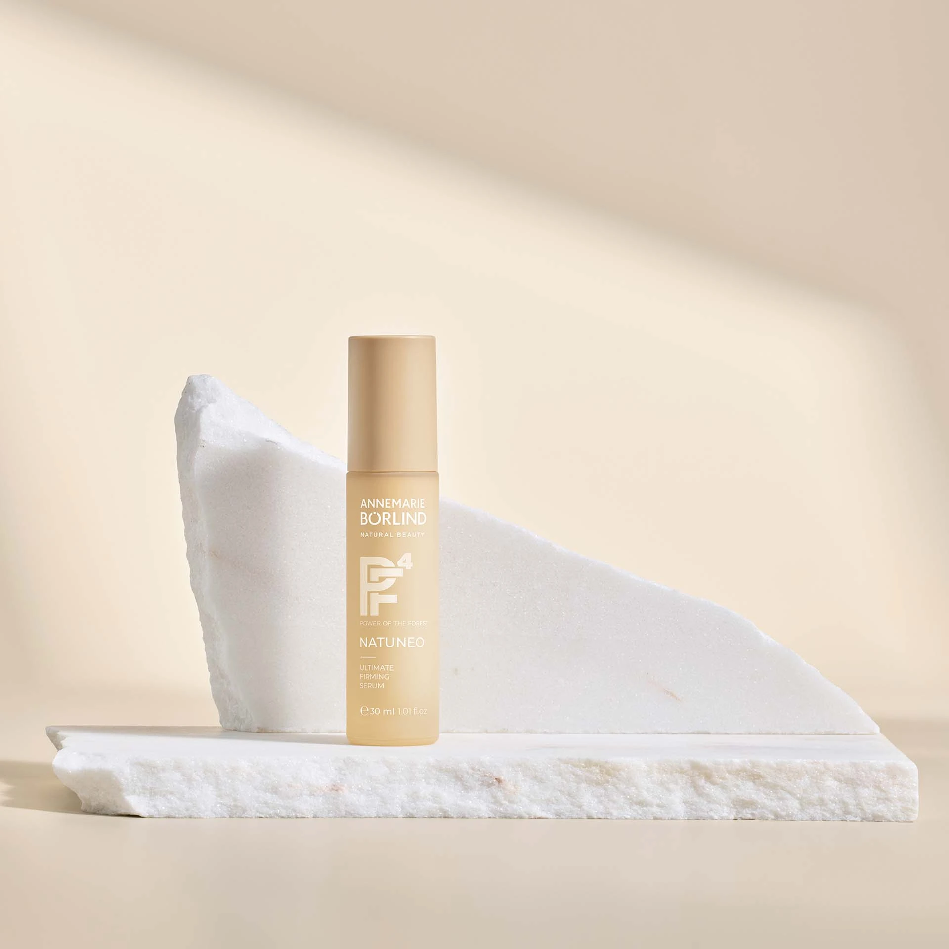 ANNEMARIE BÖRLIND NATUNEO Ultimate Firming Serum 30 ml vor weißem Marmorstein auf beigem Hintergrund