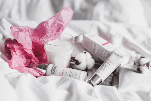 ANNEMARIE BÖRLIND Sensitiv Pflegeserie mit Creme und Spray, Glas Milch und Baumwollblüten auf weißem Stoff