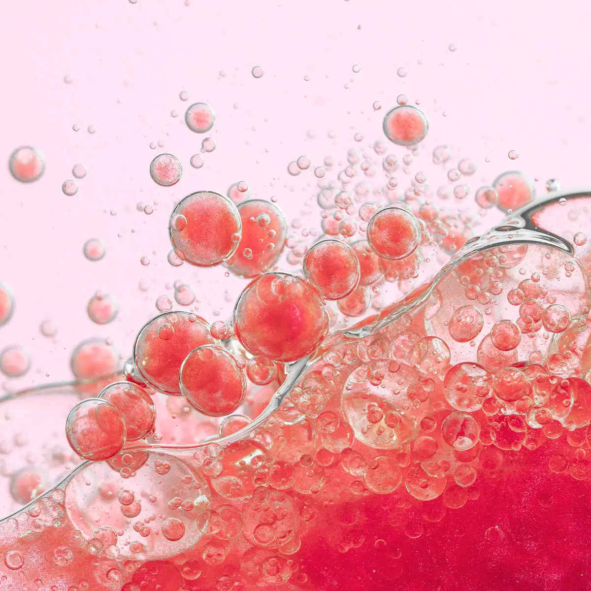 Rosa Flüssigkeit mit vielen transparenten und roten Bläschen in unterschiedlichen Größen vor hellem Hintergrund