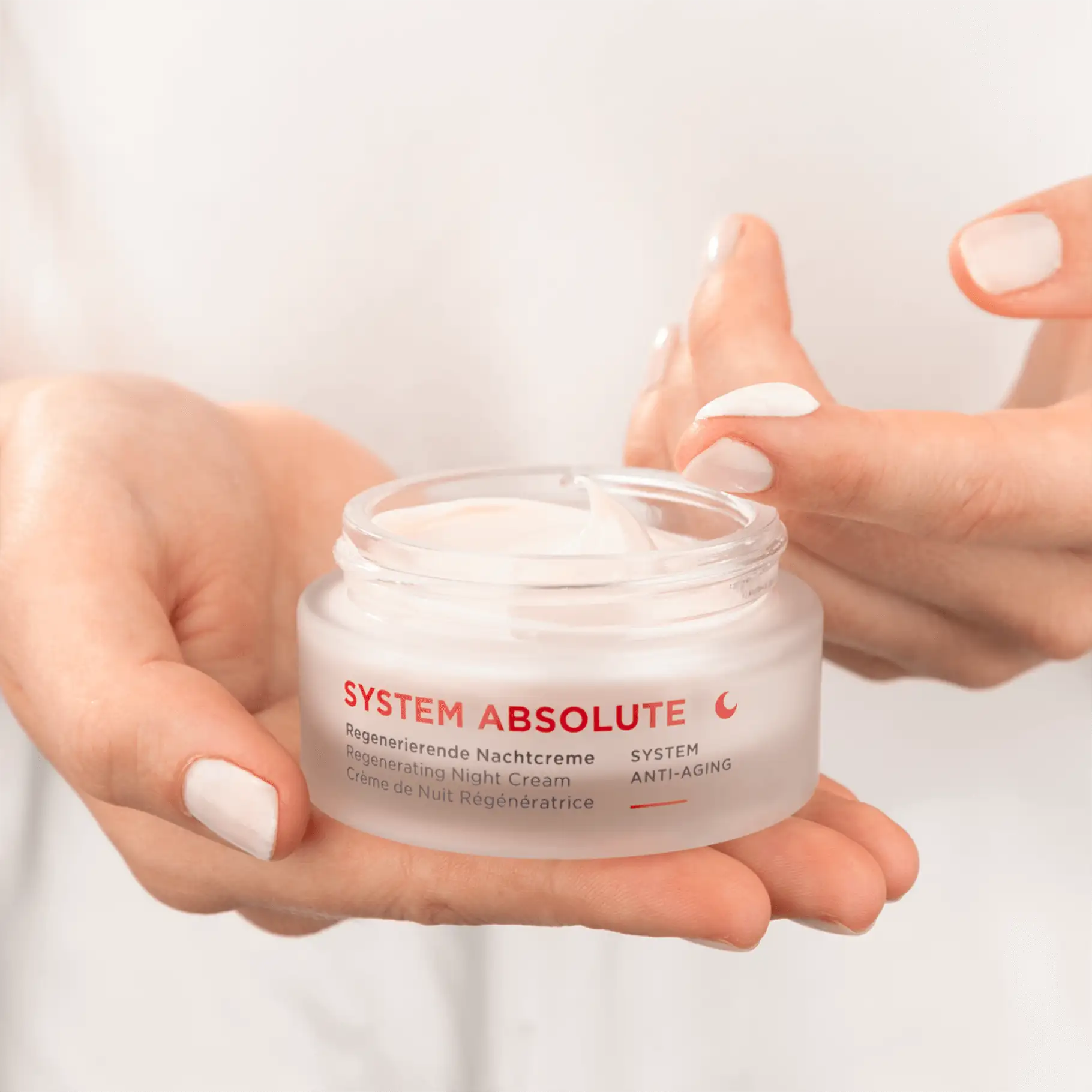 SYSTEM ABSOLUTE regenerierende Nachtcreme im geöffneten Tiegel, Creme wird mit Finger entnommen