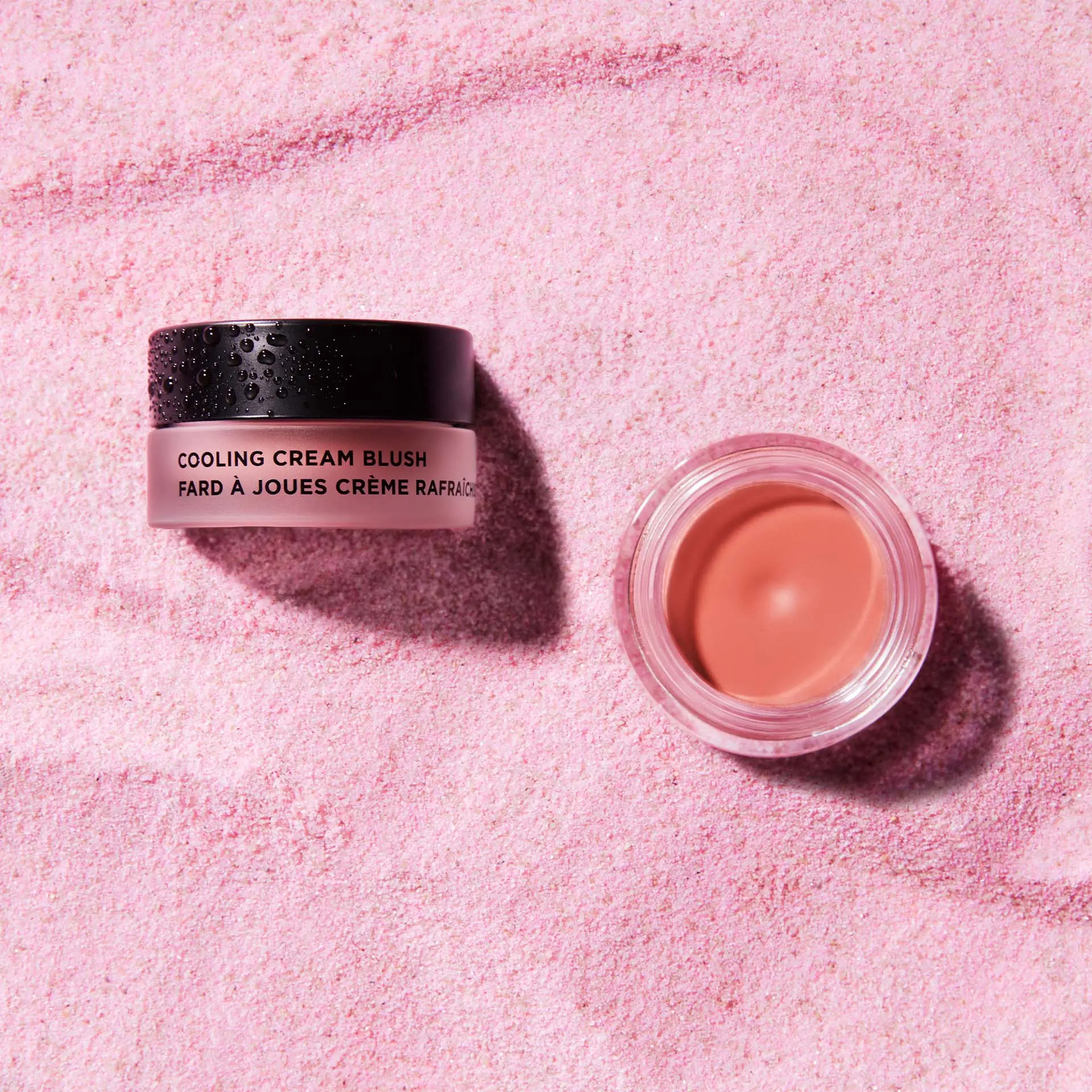COOLING CREAM BLUSH Creme-Rouge im Tiegel auf rosafarbenem, körnigem Untergrund