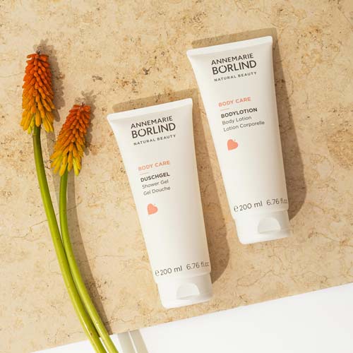 ANNEMARIE BÖRLIND Body Care Duschgel und Body Lotion je 200 ml auf hellem Stein mit roten Blüten