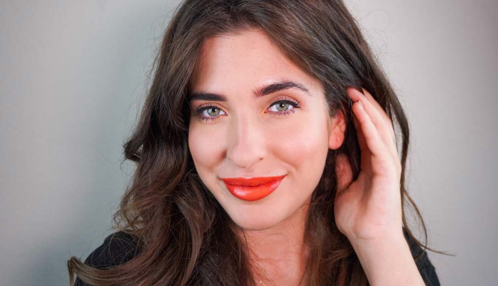 Nahaufnahme einer Frau mit oranger Lippenfarbe und leichtem Make-up, die lächelnd in die Kamera schaut