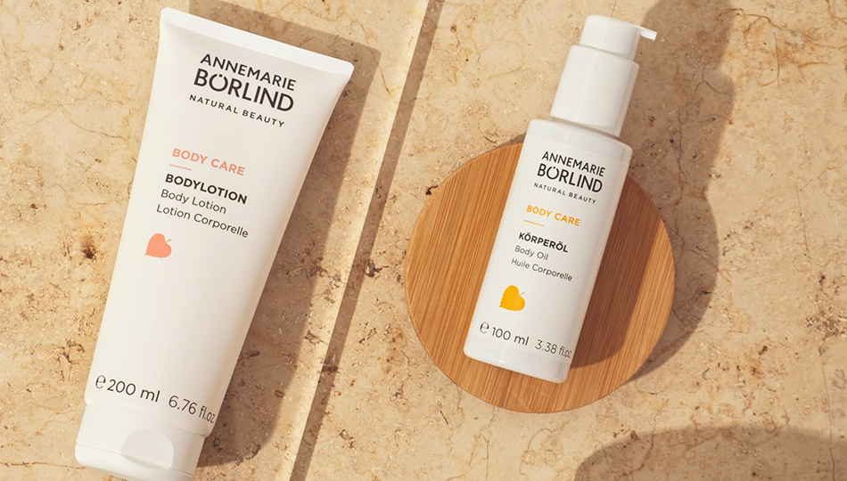 Bräune erhalten: ANNEMARIE BÖRLIND BODY CARE Bodylotion und Körperöl, inszeniert auf beigem Natursteinuntergrund.