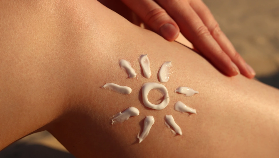 Bräune erhalten: Auf der Haut eines Beins ist eine Sonne aus Sonnencreme aufgetragen, die Schutz und Pflege für eine langanhaltende Sommerbräune symbolisiert.