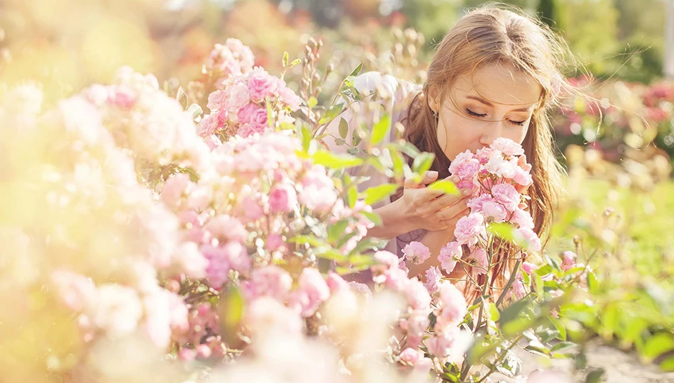 Was ist Naturkosmetik: Frau riecht an rosafarbenen Blüten in einem Garten – Sinnbild für das natürliche Dufterlebnis pflanzlicher Inhaltsstoffe.