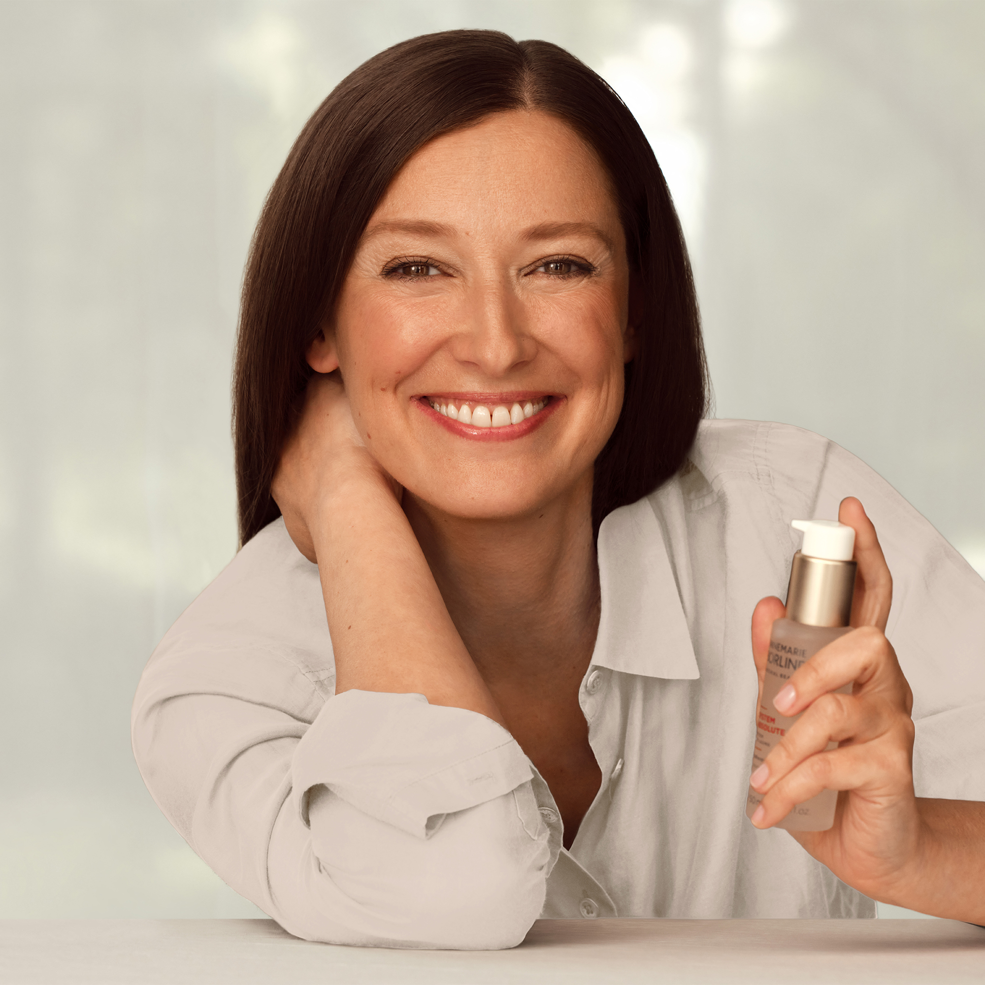 Frau lächelt entspannt und hält eine Flasche ANNEMARIE BÖRLIND SYSTEM ABSOLUTE BEAUTY Fluid