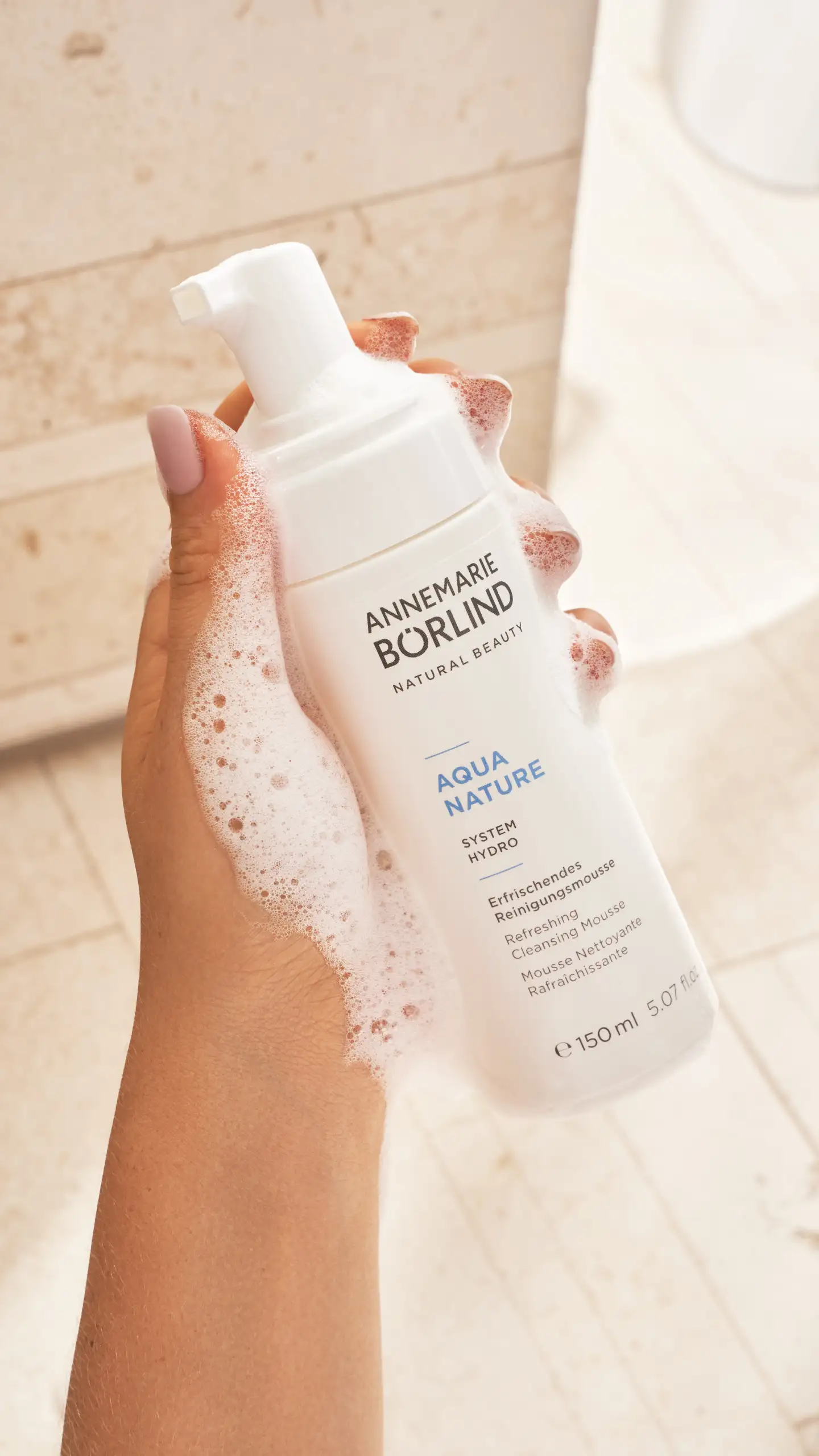 Hand hält ANNEMARIE BÖRLIND AQUA NATURE erfrischendes Reinigungsschaum mit Schaum auf Haut