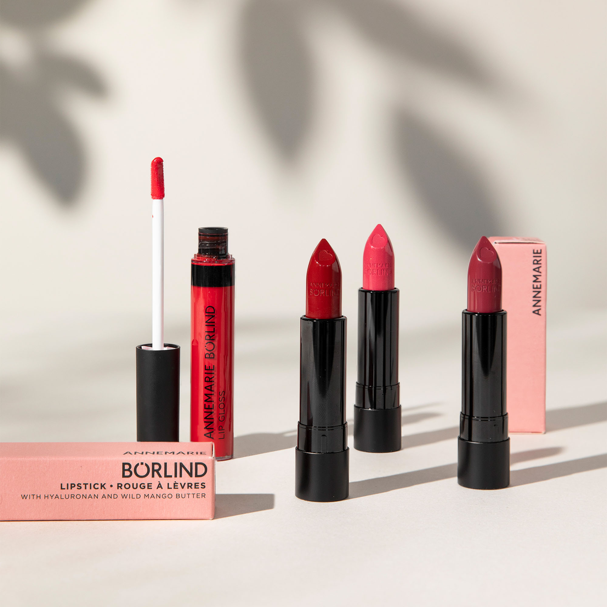 ANNEMARIE BÖRLIND Lippenstifte in drei Rottönen und Lipgloss mit Applikator vor hellem Hintergrund