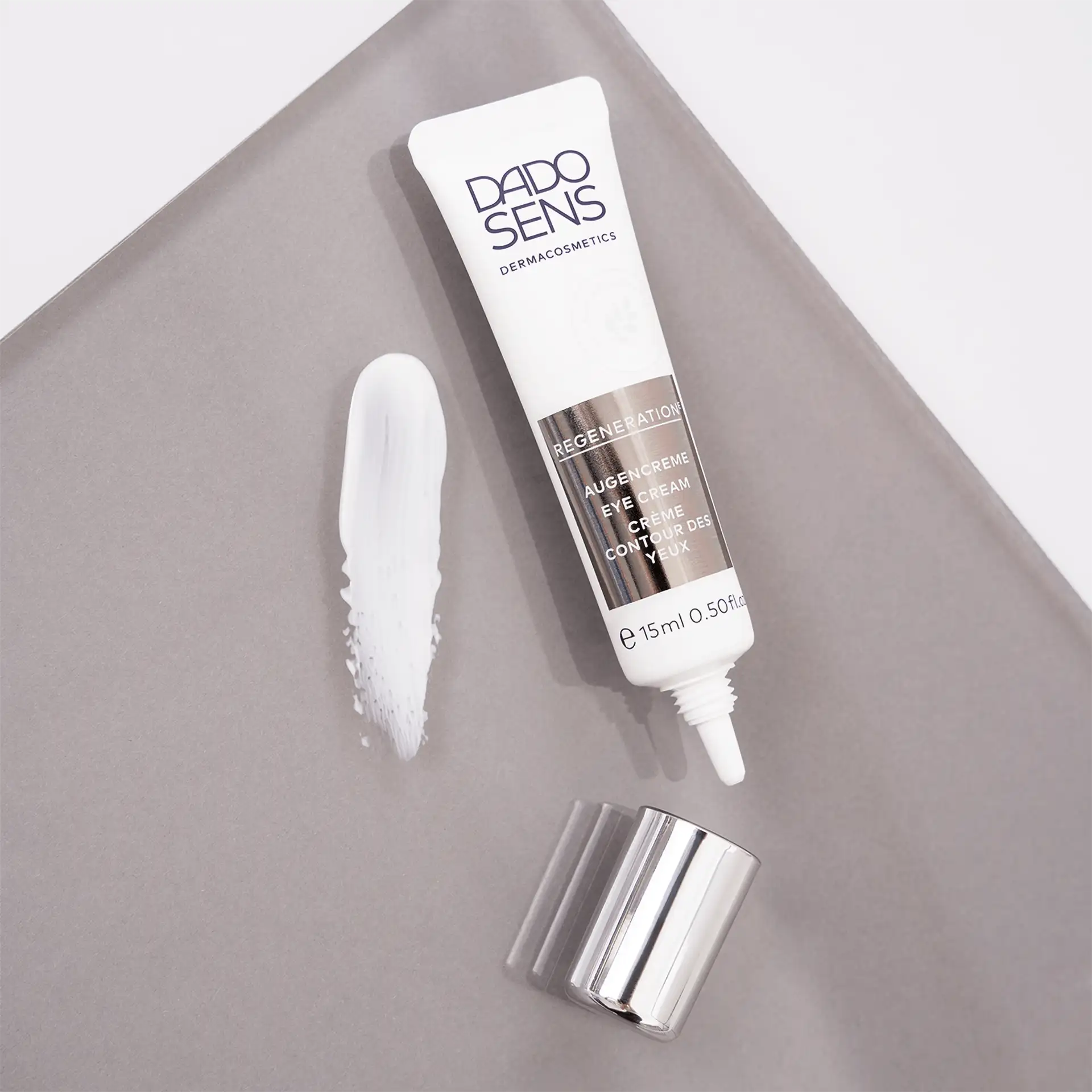 DADO SENS Regeneration Augencreme 15 ml Tube mit Cremeprobe auf grauem Untergrund