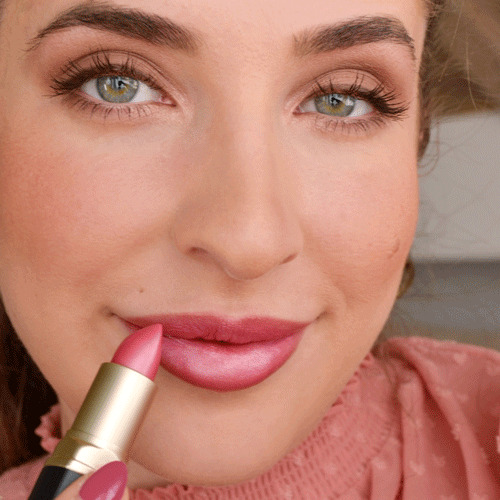 Frau trägt rosa Lippenstift auf, Nahaufnahme mit betonten Augen und natürlichem Make-up im warmen Licht