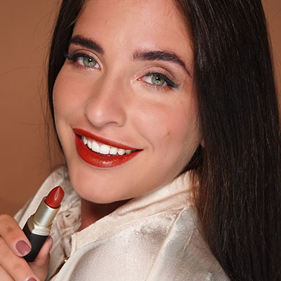 Frau lächelt mit rotem Lippenstift, hält Lippenstift in der Hand, Nahaufnahme, warme Lichtstimmung