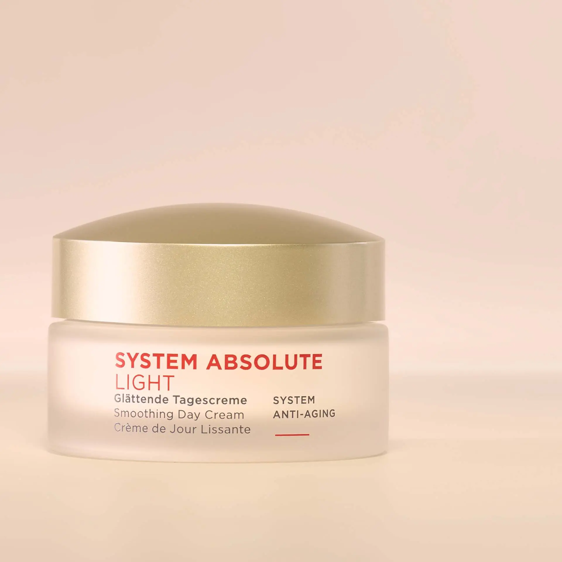 SYSTEM ABSOLUTE LIGHT glättende Tagescreme im transparenten Tiegel mit goldenem Deckel vor beigem Hintergrund