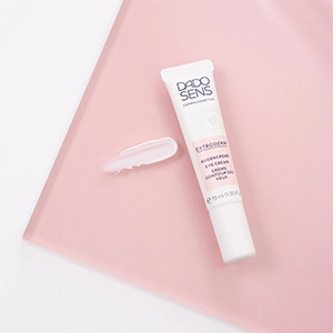 Augencreme für empfindliche Augen: DADO SENS EXTRODERM Eye Cream Tube mit einer Probe der cremigen Textur, inszeniert auf rosafarbenem Untergrund.