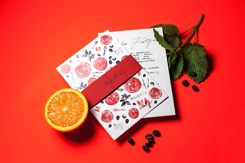 Grußkarte mit roten Illustrationen, halbierte Orange, Kaffeebohnen und grünes Minzblatt auf rotem Hintergrund