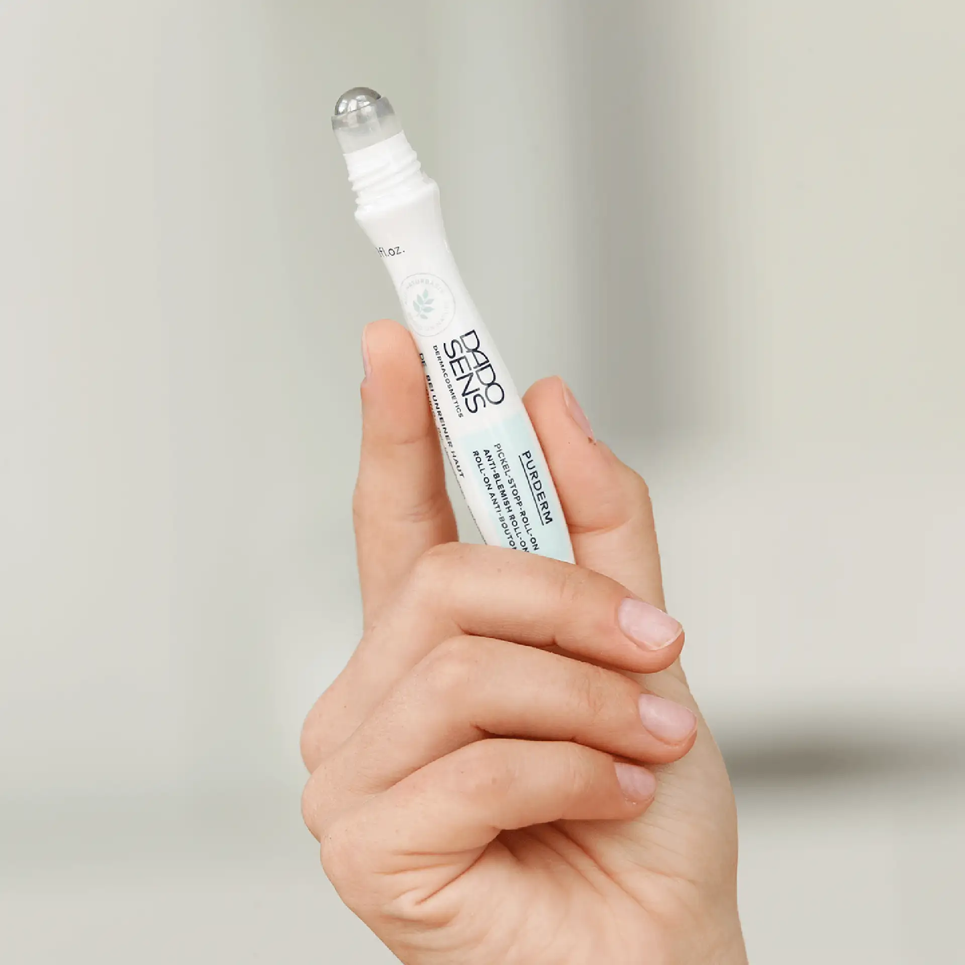 Hand hält DADO SENS PURDERM Pickel-Stop Roll-on 10 ml mit Metall-Applikator vor hellem Hintergrund