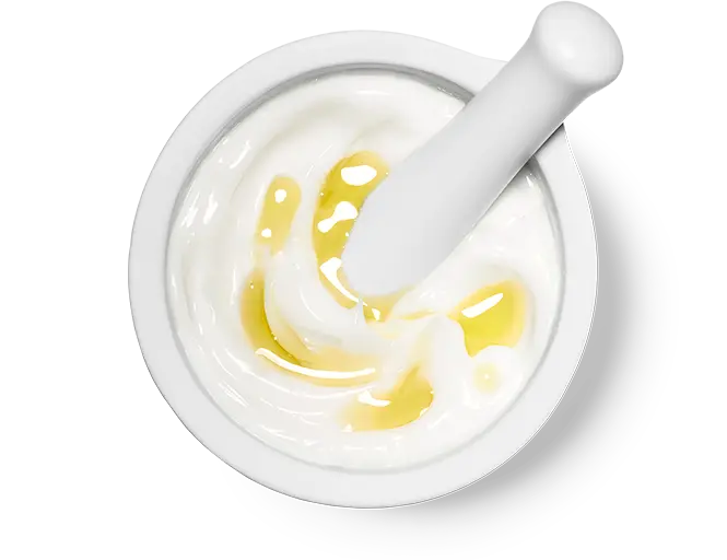 Mörser mit weißer Creme und gelbem Öl, Stößel rührt die Mischung homogen um