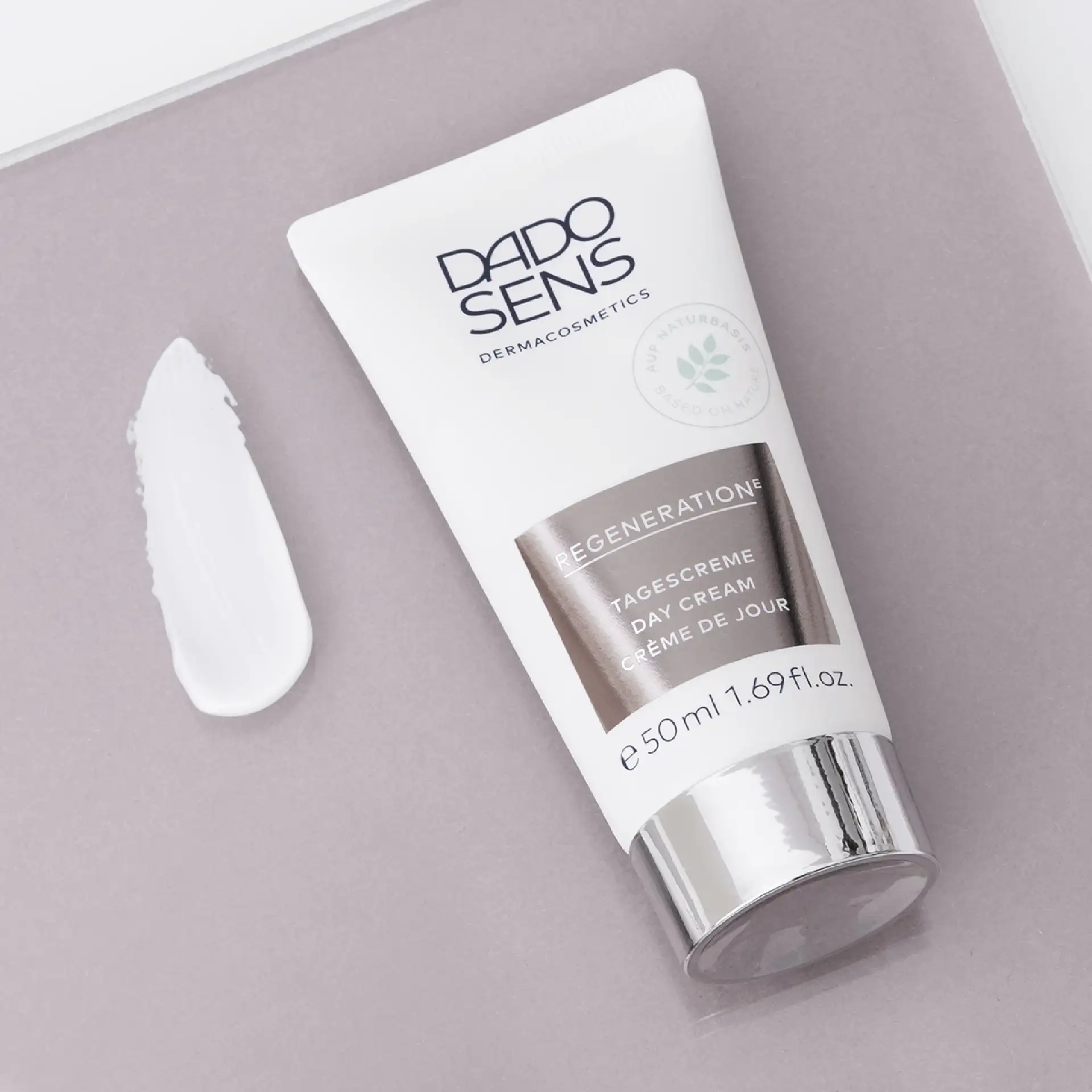 DADO SENS Regeneration E Tagescreme 50 ml Tube mit silbernem Deckel und Cremeprobe auf grauem Untergrund