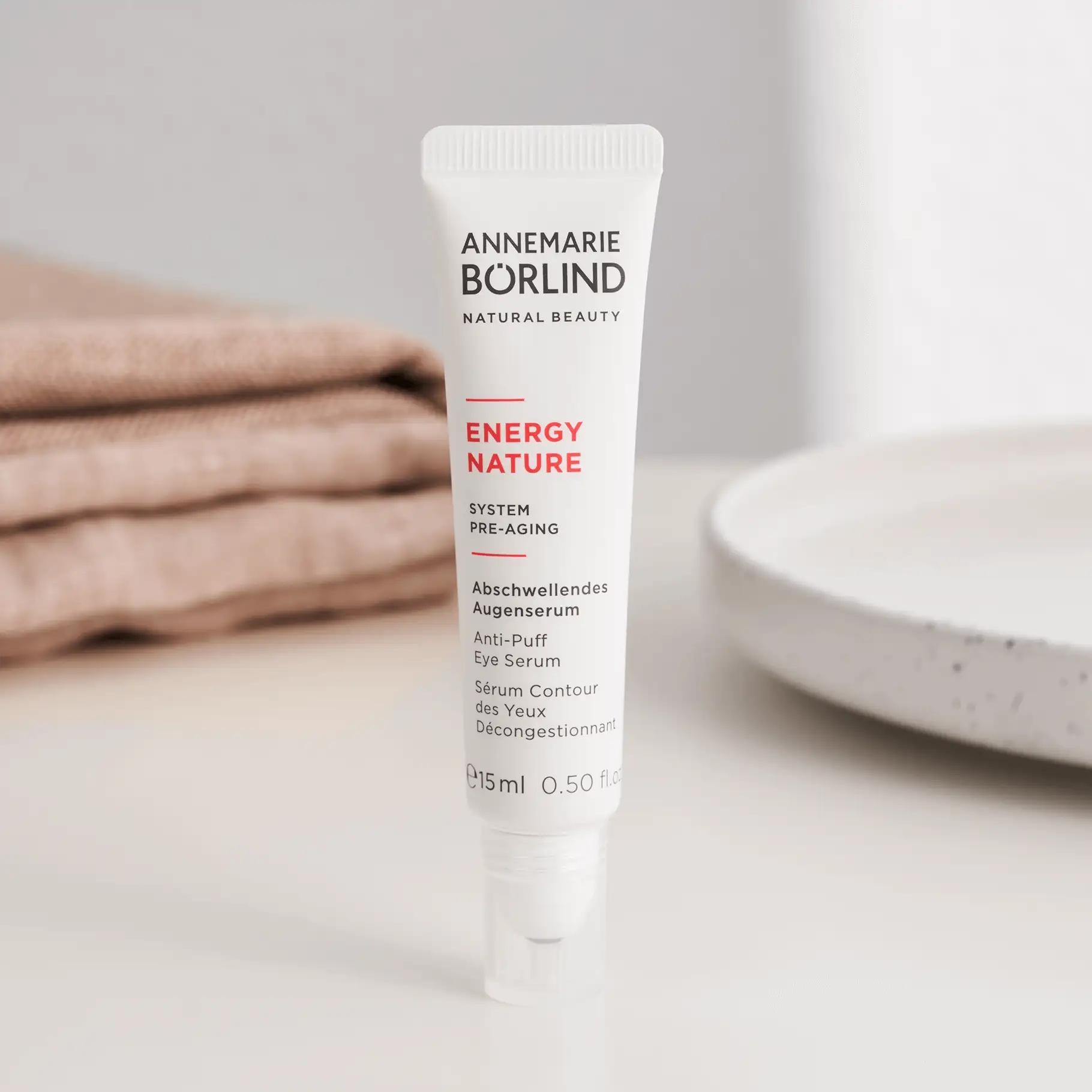 ANNEMARIE BÖRLIND Energy Nature abschwellendes Augenserum in weißer Tube, 15 ml, vor beigem Stoff und Teller