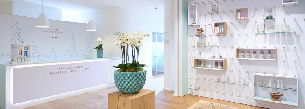 Empfangsbereich des ANNEMARIE BÖRLIND NATURAL BEAUTY SPA mit Produktregalen und blühender Orchidee in blauem Topf