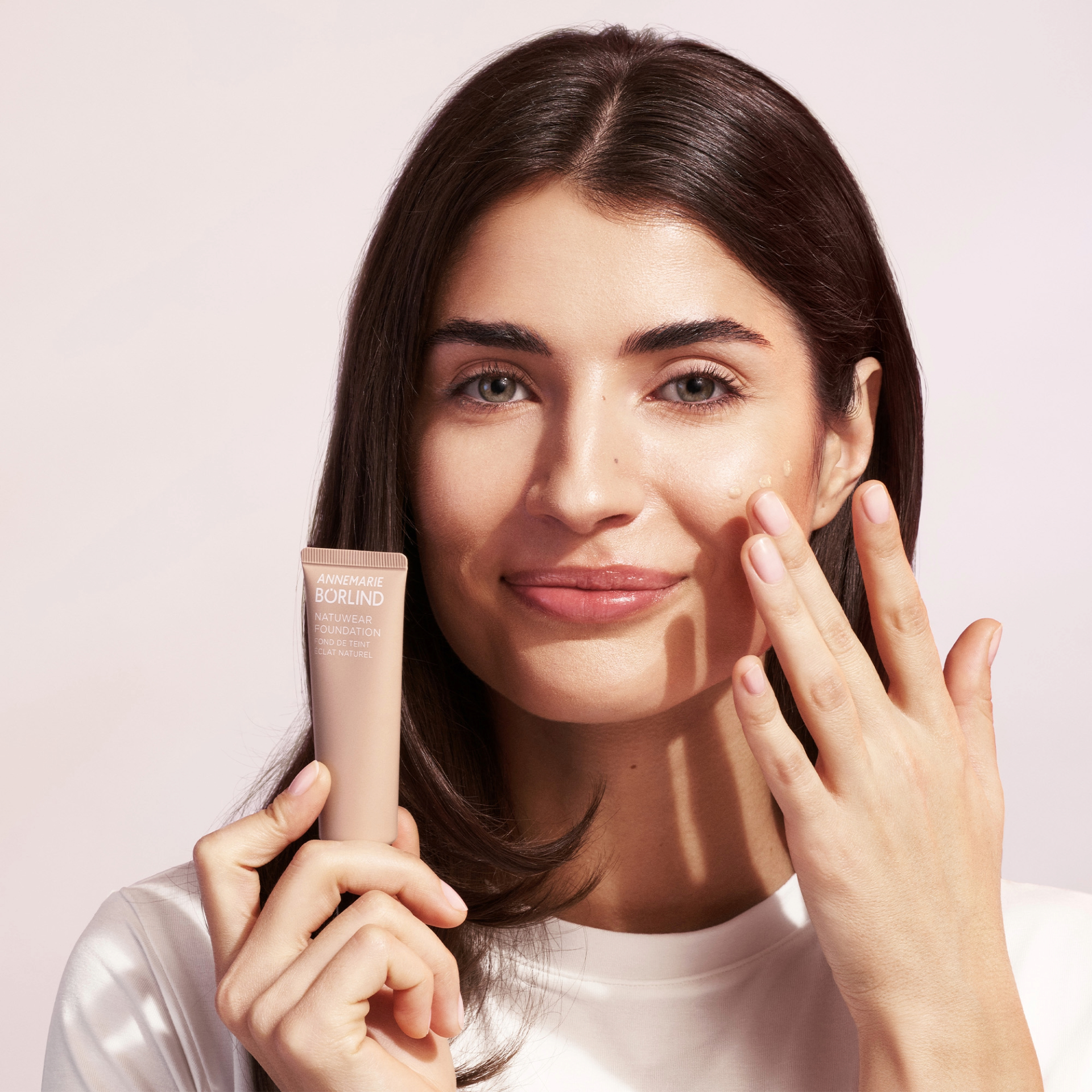 Frau trägt ANNEMARIE BÖRLIND NATUWEAR FOUNDATION auf Wange auf, hält Tube in der Hand