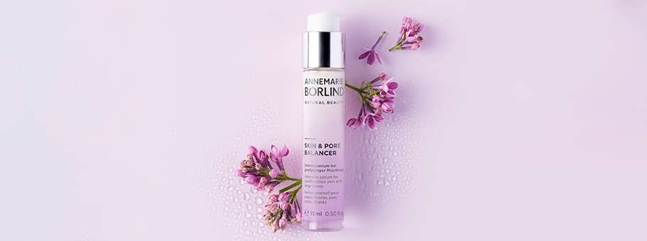 ANNEMARIE BÖRLIND Skin & Pore Balancer Serum mit Flieder, umgeben von lila Blüten auf hellviolettem Hintergrund