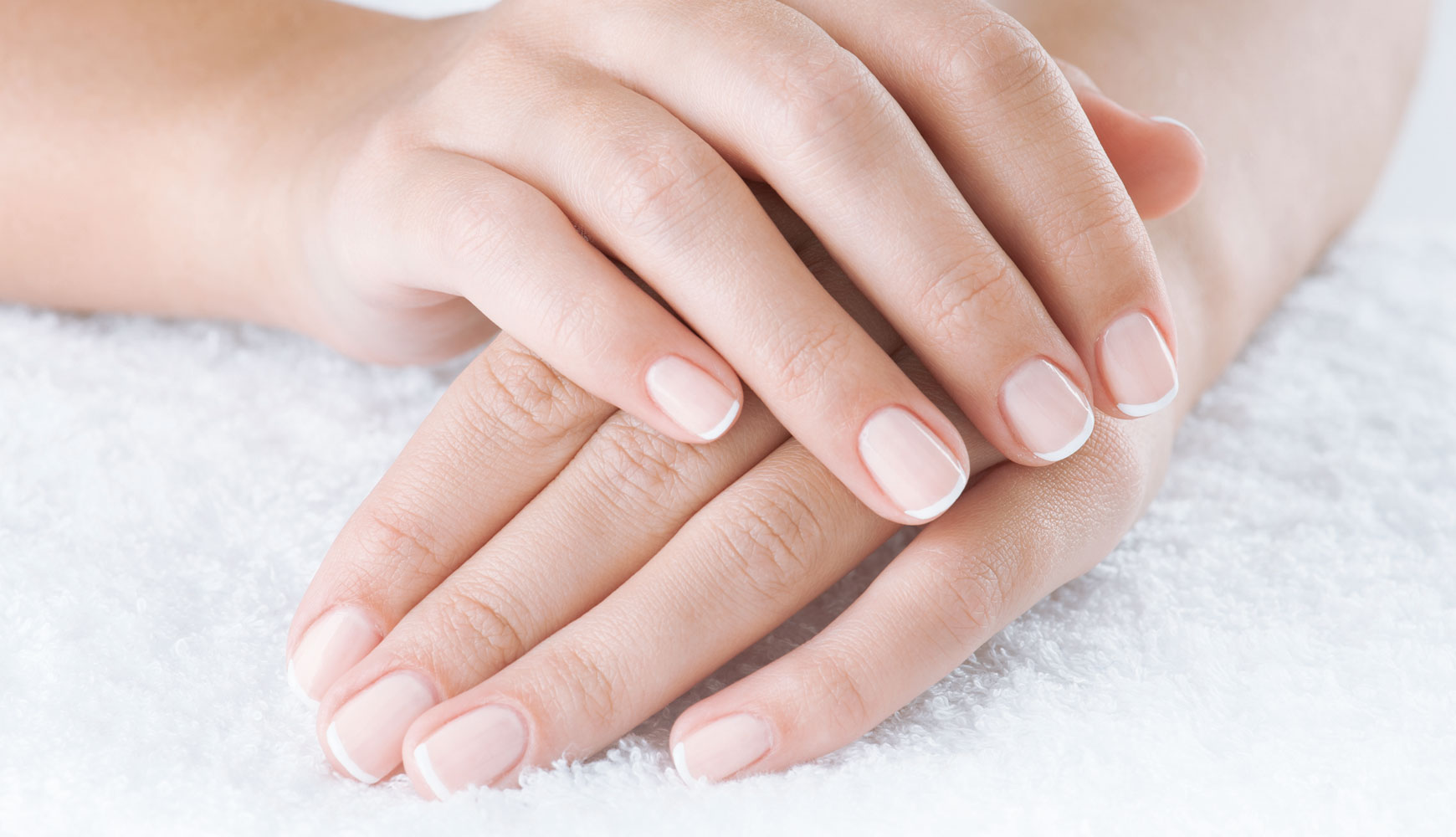 Zwei Hände mit gepflegten Fingernägeln und klassischer French-Maniküre auf weißem Handtuch