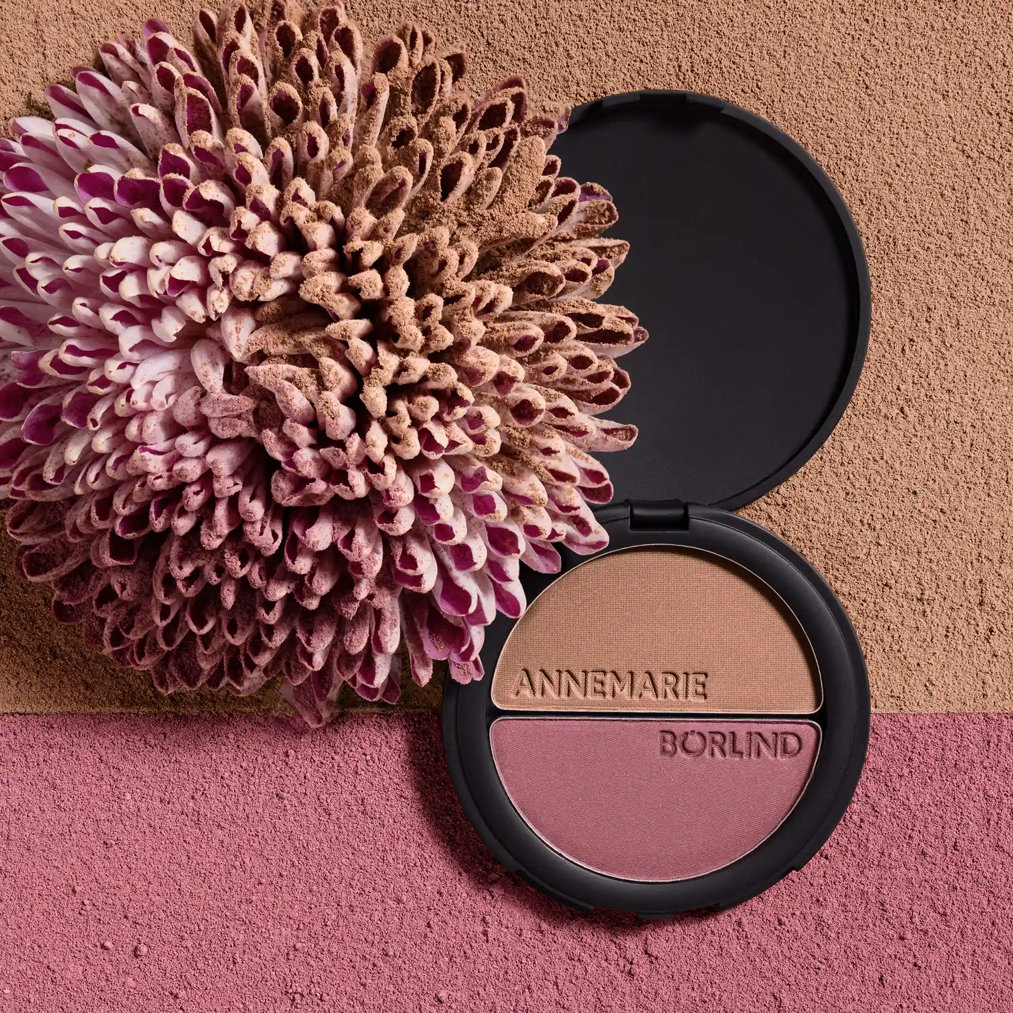 ANNEMARIE BÖRLIND 2IN1 BRONZER & SOFT BLUSH in schwarzer Dose, dekorativ mit Blume auf braun-rosa Puderkulisse