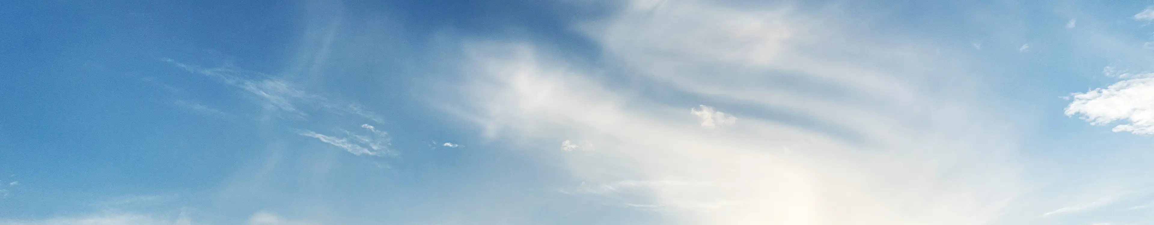 Blauer Himmel mit weißen, dünnen Wolken und Sonnenlicht, das von rechts unten scheint