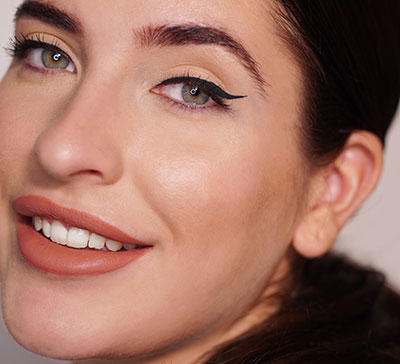 Nahaufnahme eines lächelnden Gesichts mit betontem Lidstrich und dezentem Make-up bei abfallendem Auge